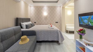 Une chambre d’hôtel moderne avec un canapé, un lit recouvert d’une couvre-lit à motifs, un téléviseur à écran plat fixé au mur et un vase avec des fleurs placé sur une table d’appoint.