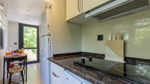 Une cuisine moderne dotée d’une cuisinière intégrée, un coin repas avec une table et des chaises, et une vue sur la verdure environnante.