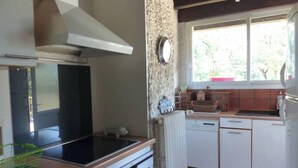 A kitchen with white cabinets, a stove, a sink, and a window with a view of greenery outside. - Large campane house (Brignac-la-Plaine)