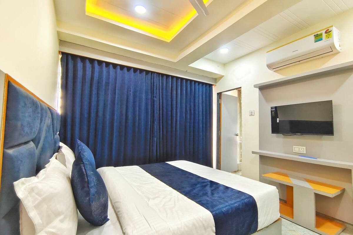Quarto de hotel com cama, televisão, ar condicionado e cortina.