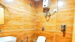 A bathroom with a wooden floor, a white toilet, a bidet, a sink, and a mirror. - Hotel Krishna Park  (Ahmedabad)