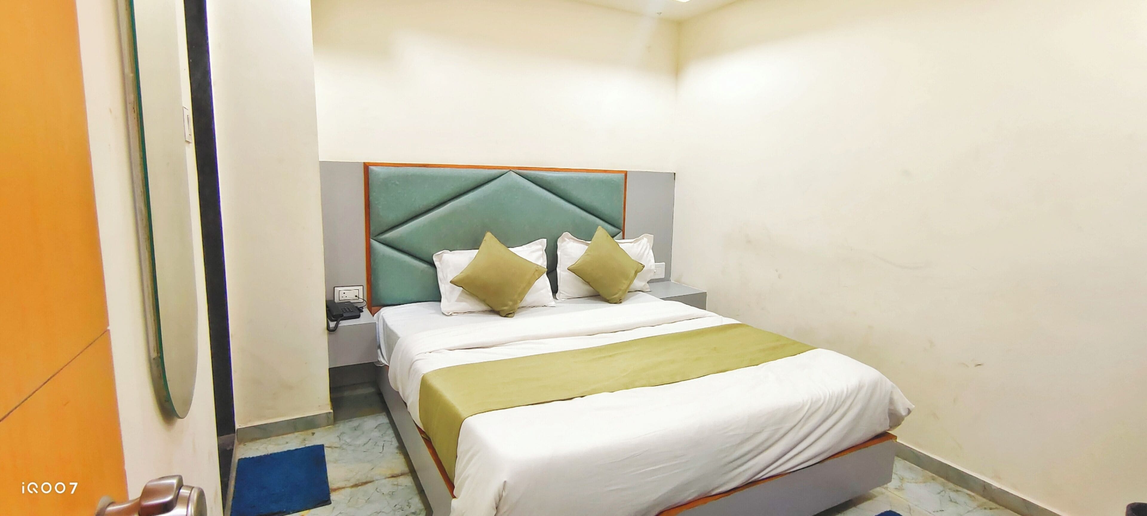 A hotel room with a bed, a nightstand, a telephone, and a mirror.