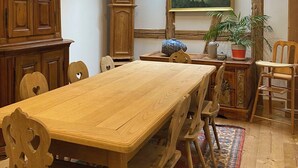 A dining room with a wooden table, chairs, a clock, a painting, and a potted plant.