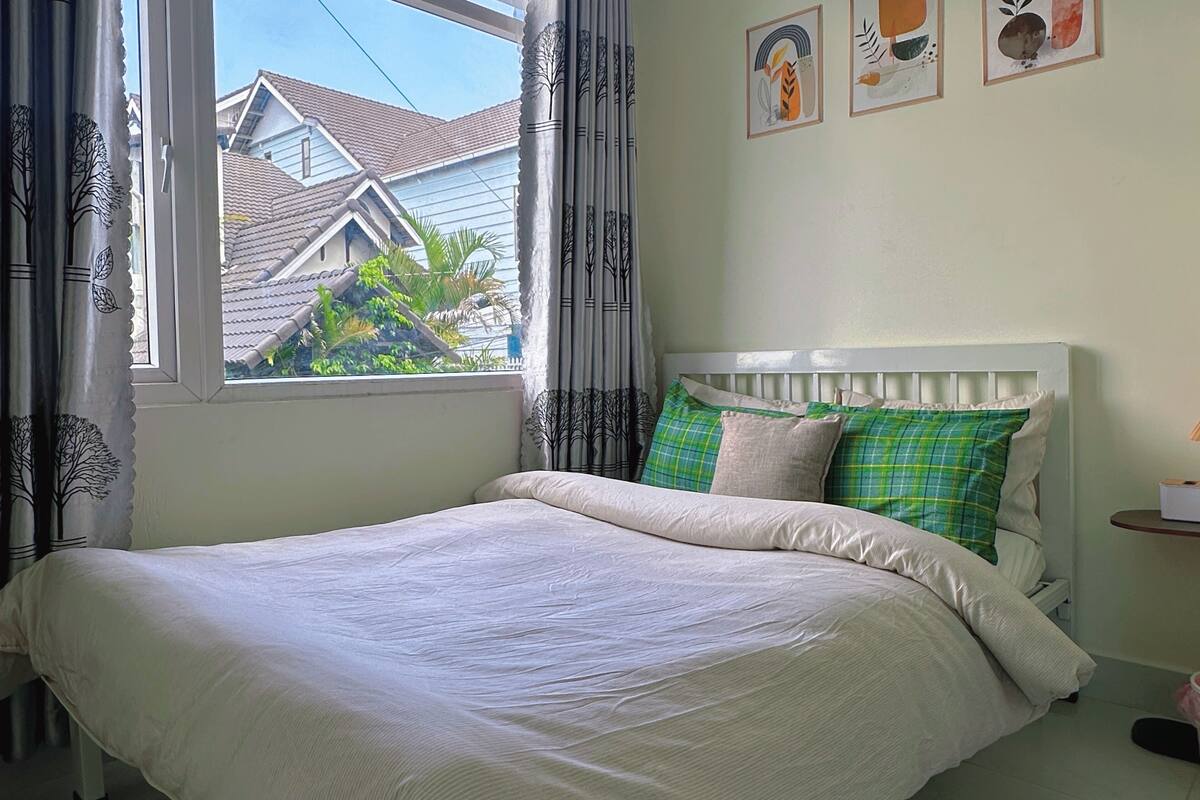 A bedroom with a bed, curtains, a window, and a wall with framed artwork.