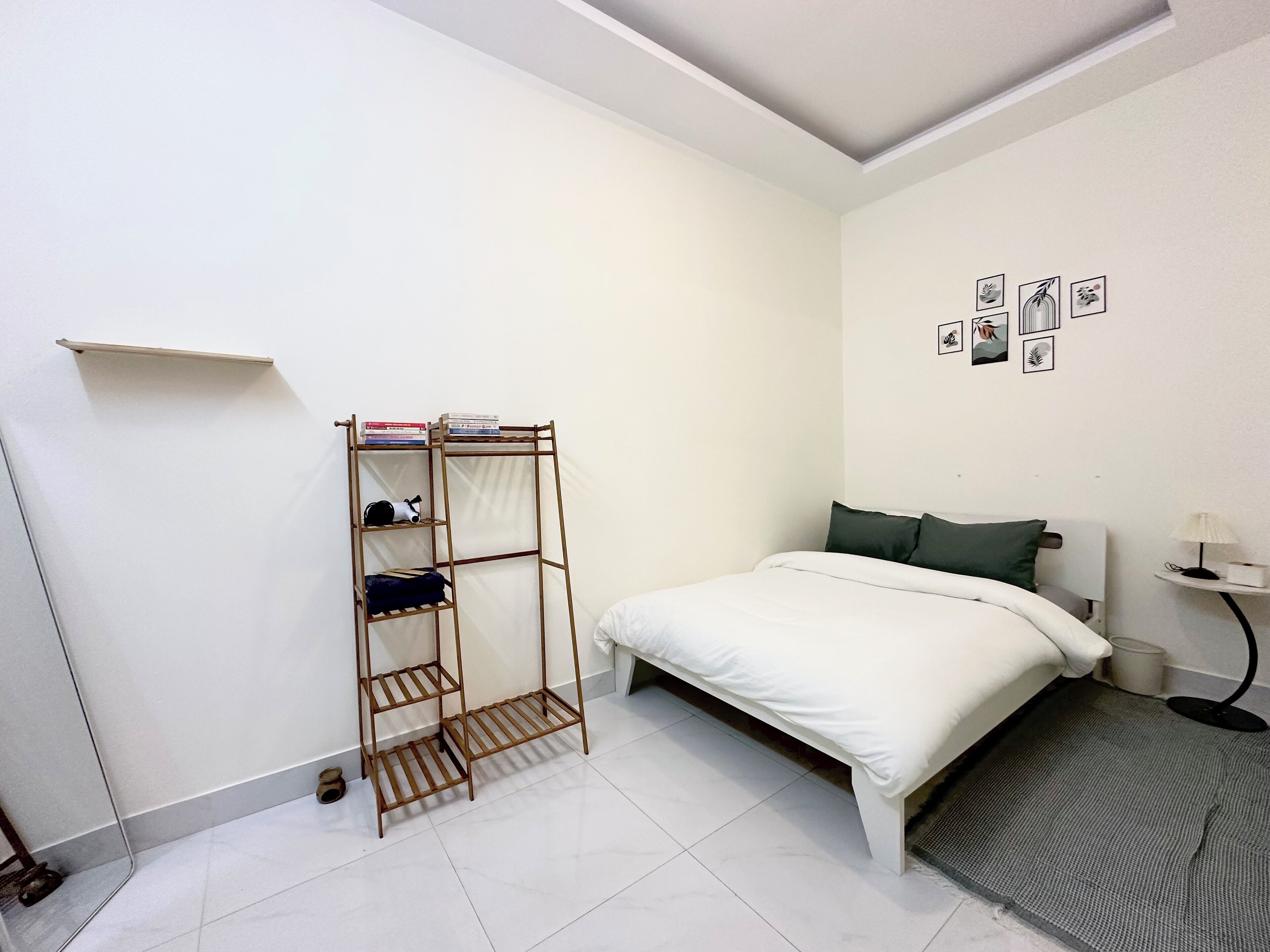 Une chambre à coucher avec un lit, une étagère en bois remplie de livres, une petite table avec une lampe et un mur orné de tableaux encadrés.