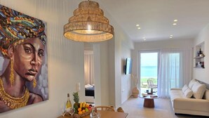 A modern living room with a dining area, a large painting, and a view of the sea. - JM Dēos Suites (Viannos)