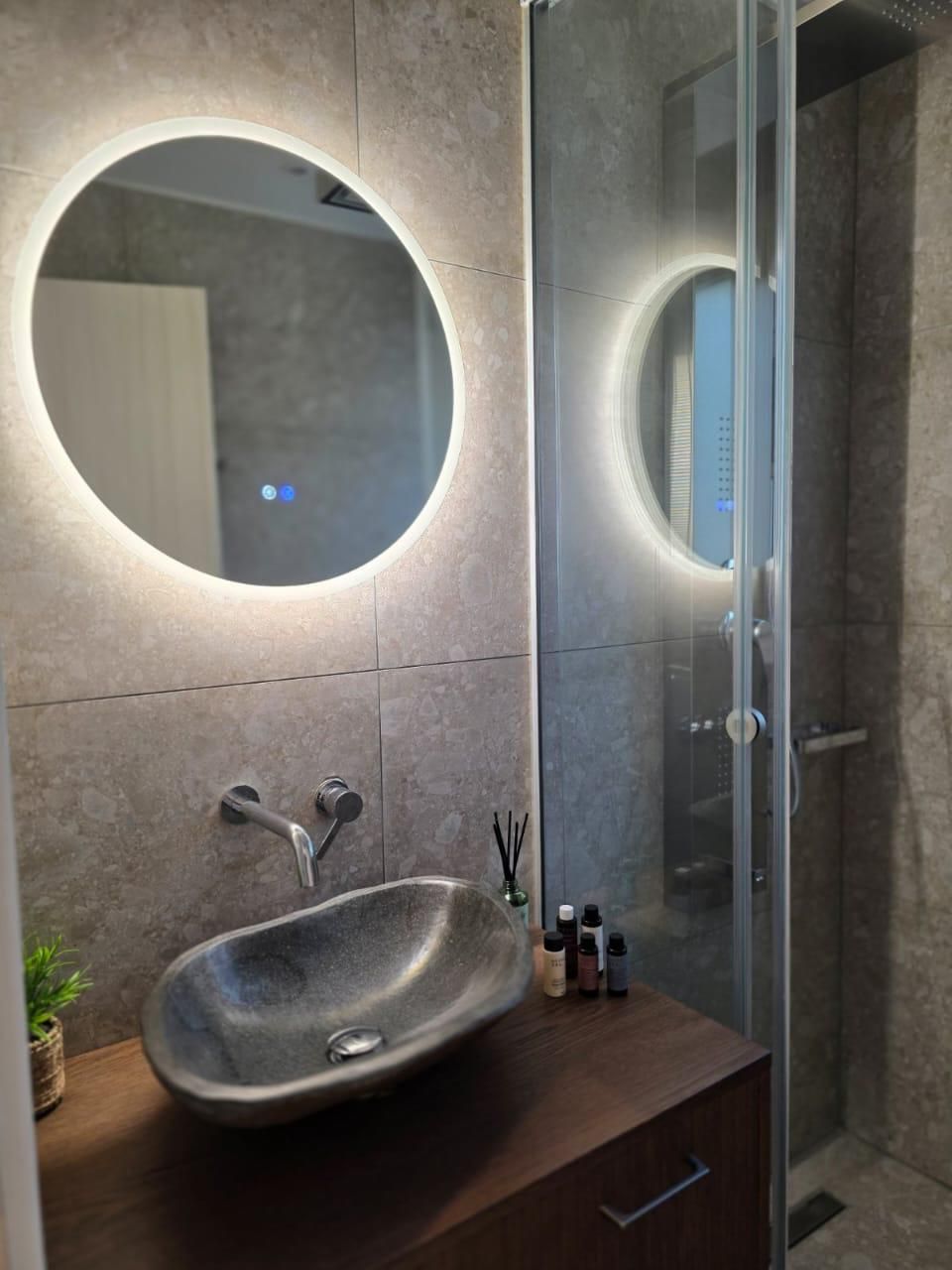 A modern bathroom with a round mirror, a vessel sink, and a glass-enclosed shower.