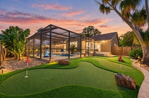 Una casa moderna con un patio con vidrio, una piscina y un campo de mini golf.
