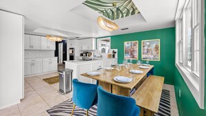A modern kitchen with white cabinets, a central island, and a dining area with blue chairs and a wooden table set for six.