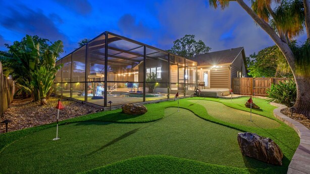 A modern house with a glass-enclosed patio, a swimming pool, and a well-maintained lawn.