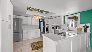 A modern kitchen with white cabinets, a central island, stainless steel appliances, and a unique ceiling design.