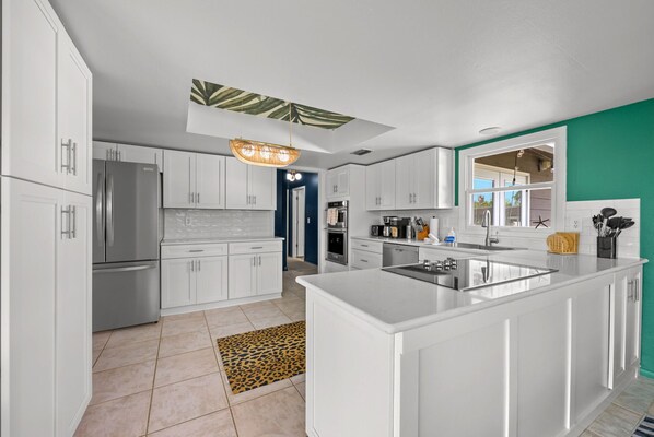 A modern kitchen with white cabinets, a central island, stainless steel appliances, and a unique ceiling design. - Family Retreat | Pool | Putt Putt | Playground (Bradenton)