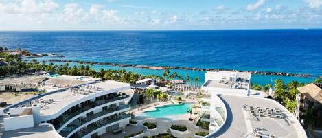 A resort with a central pool, multiple balconies, and a view of the ocean.