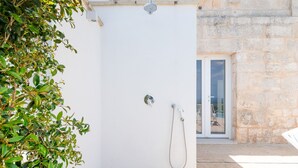 A white outdoor shower with a hose, a stone wall, and a door with a glass panel.
