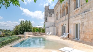 A pool area with lounge chairs and a stone building with arched windows.