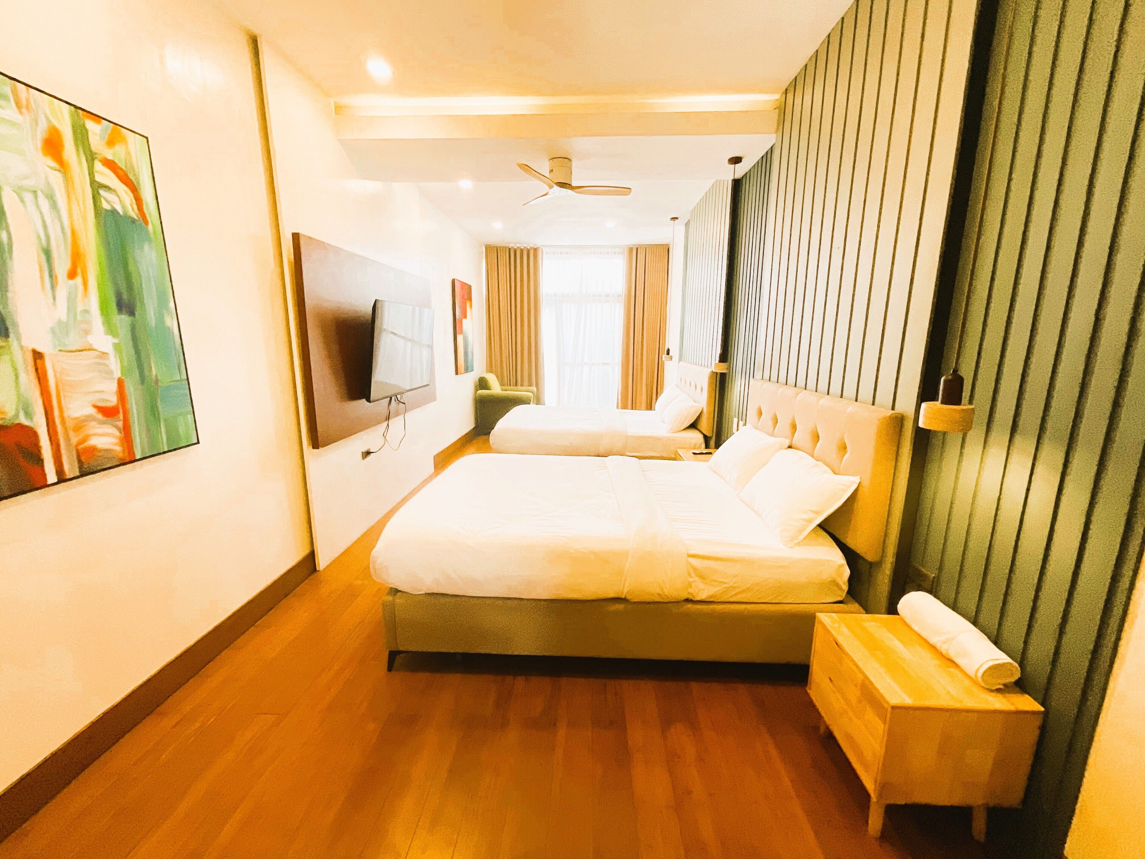 A hotel room with a large bed, a smaller bed, a TV, a wooden bench, and a painting on the wall.
