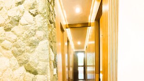 Un pasillo con pared de piedra, suelo de madera y una silla blanca.