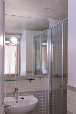 A bathroom with a glass shower enclosure, a sink with a mirror above it, and tiled walls.
