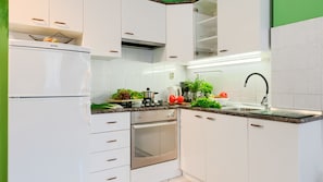 A modern kitchen with white cabinets, a built-in oven, a stainless steel sink, and a variety of fresh vegetables on the counter.