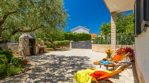 A sunny courtyard with a stone wall, a small stone structure, and a lounge chair with a yellow blanket.