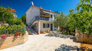 A two-story house with a balcony, a staircase, and a garden area with potted plants and outdoor furniture.