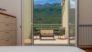 A balcony with a mountain view, a dining table, two chairs, and a sofa.