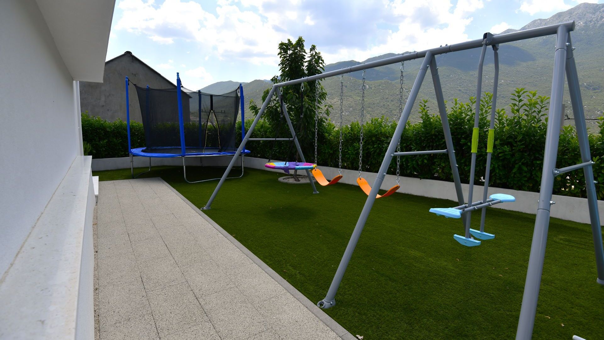 Une terrasse avec un trampoline, une balançoire et une pelouse artificielle.