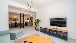 Una sala de estar moderna con una televisión, una mesa de centro de madera, un sofá y una cocina al fondo.