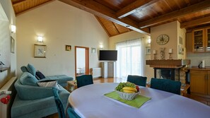 A spacious living room with a high ceiling, a television, a fireplace, and a dining area with a fruit basket. - Villa Panorama Hill by Villas Guide (Cestica)