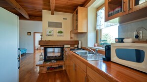 Une cuisine avec des meubles en bois, un four à micro-ondes encastré, une cuisinière à gaz et une cheminée en briques.