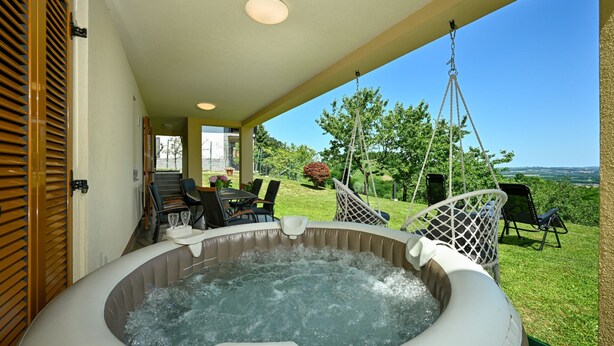 Un bain à remous sur une terrasse couverte, avec des sièges d’extérieur et une vue sur la campagne.
