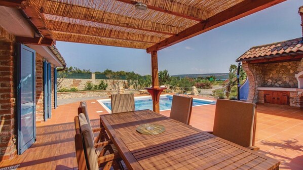 A covered outdoor area with a pool, wooden furniture, and a stone fireplace.