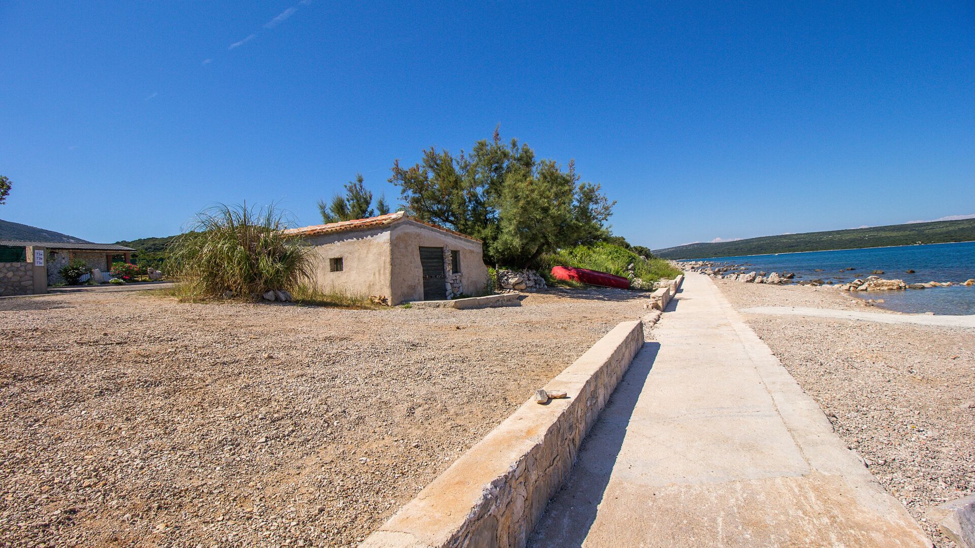 A coastal property with a gravel path leading to a small building, a red kayak, and a clear view of the sea.