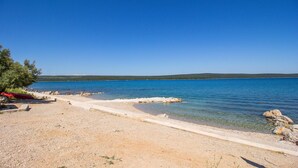 Une plage dégagée avec un sentier de gravier menant à l’eau, un kayak rouge et un pin.