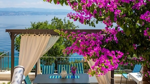 A covered outdoor seating area with a table and chairs, overlooking a body of water.