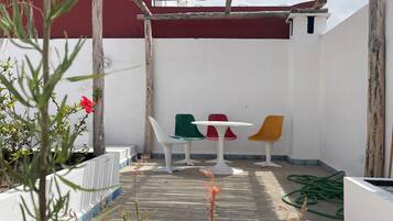 Un patio con una pérgola de madera, sillas blancas y coloridas, y una variedad de plantas, entre ellas suculentas.