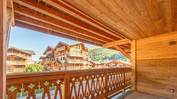 Un balcon en bois orné de balustrades complexes, donnant sur une région montagneuse parsemée de nombreux bâtiments en bois.