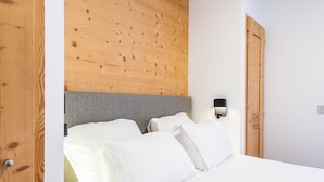 Un lit bien fait, avec du linge de lit blanc, une tête de lit grise et un mur recouvert de panneaux en bois au-dessus.
