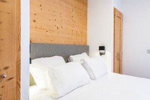 Een netjes opgemaakt bed met witte lakens, een grijze hoofdbord en een houten paneelwand erboven.