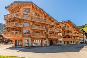 A multi-story wooden building with balconies, a stone entrance, and a clear sky.