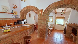 Een keuken met bakstenen muren, een betegelde vloer, een bar met krukken en een eettafel met stoelen.
