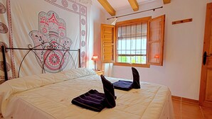 Een slaapkamer met een bed, een raam met houten luiken, een wandtapijt aan de muur en een lamp op een nachtkastje.
