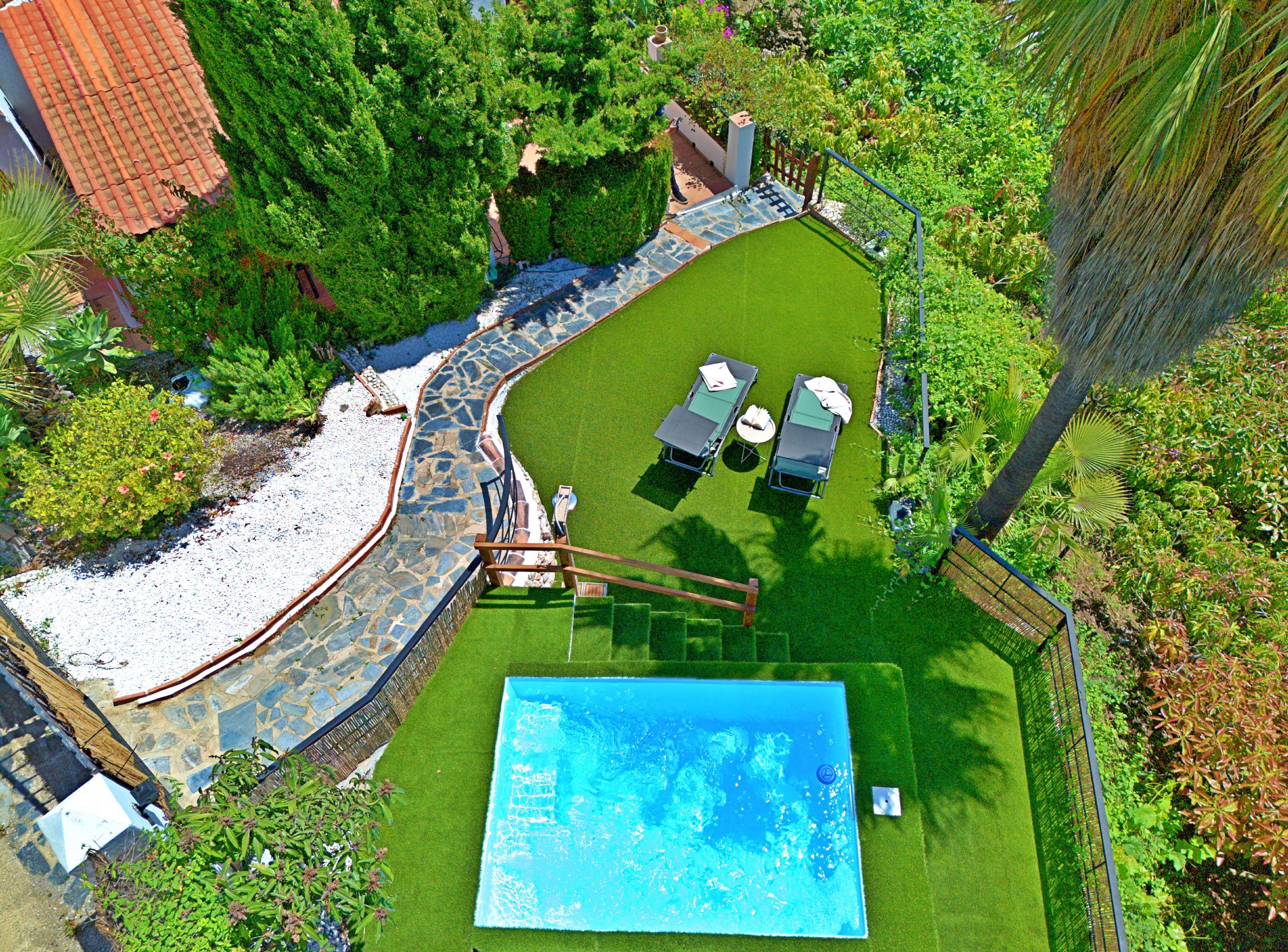 Una piscina rodeada por un solárium de piedra, con un pequeño patio y dos sillas reclinables.