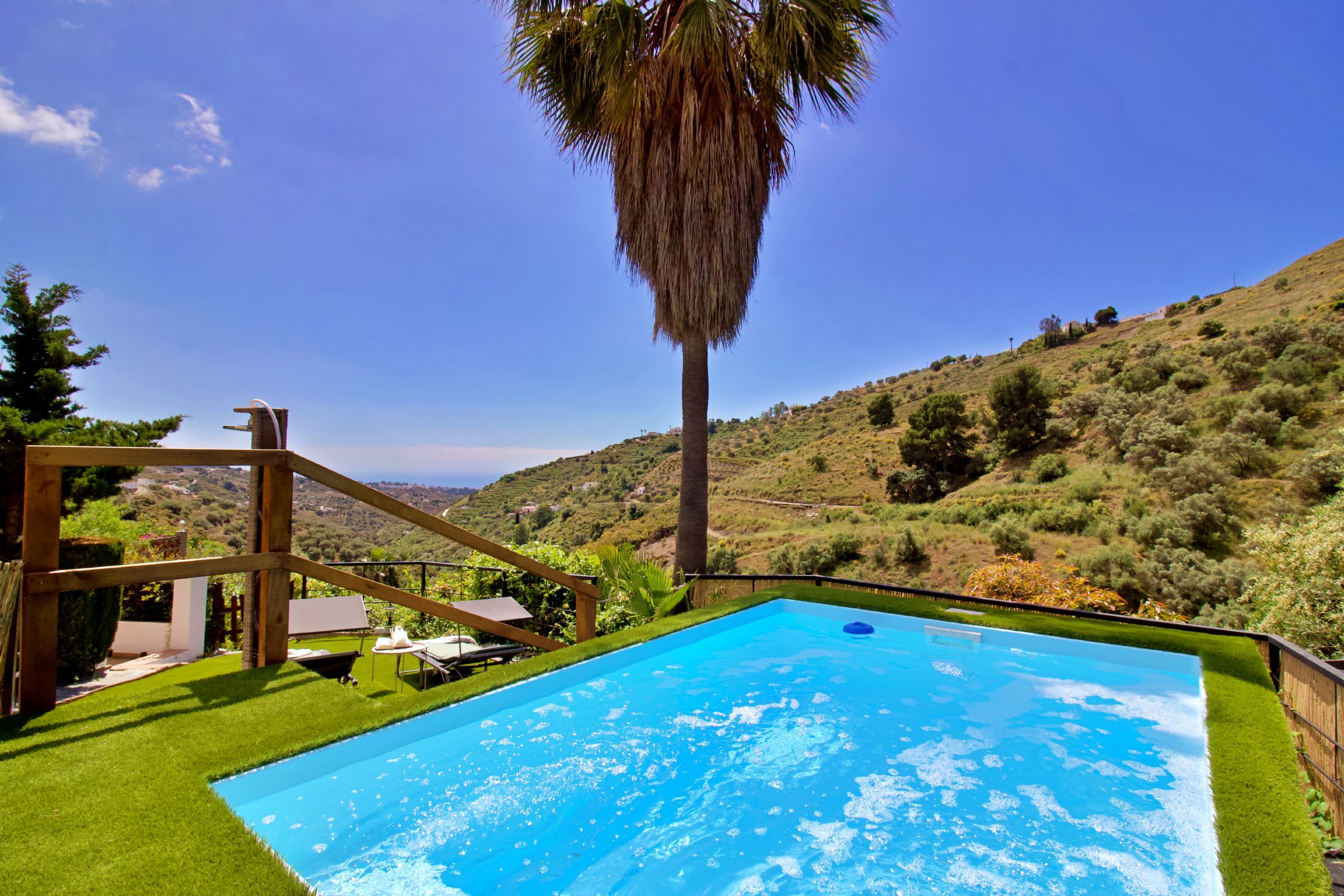 A swimming pool with a wooden deck, surrounded by lush greenery and hills.