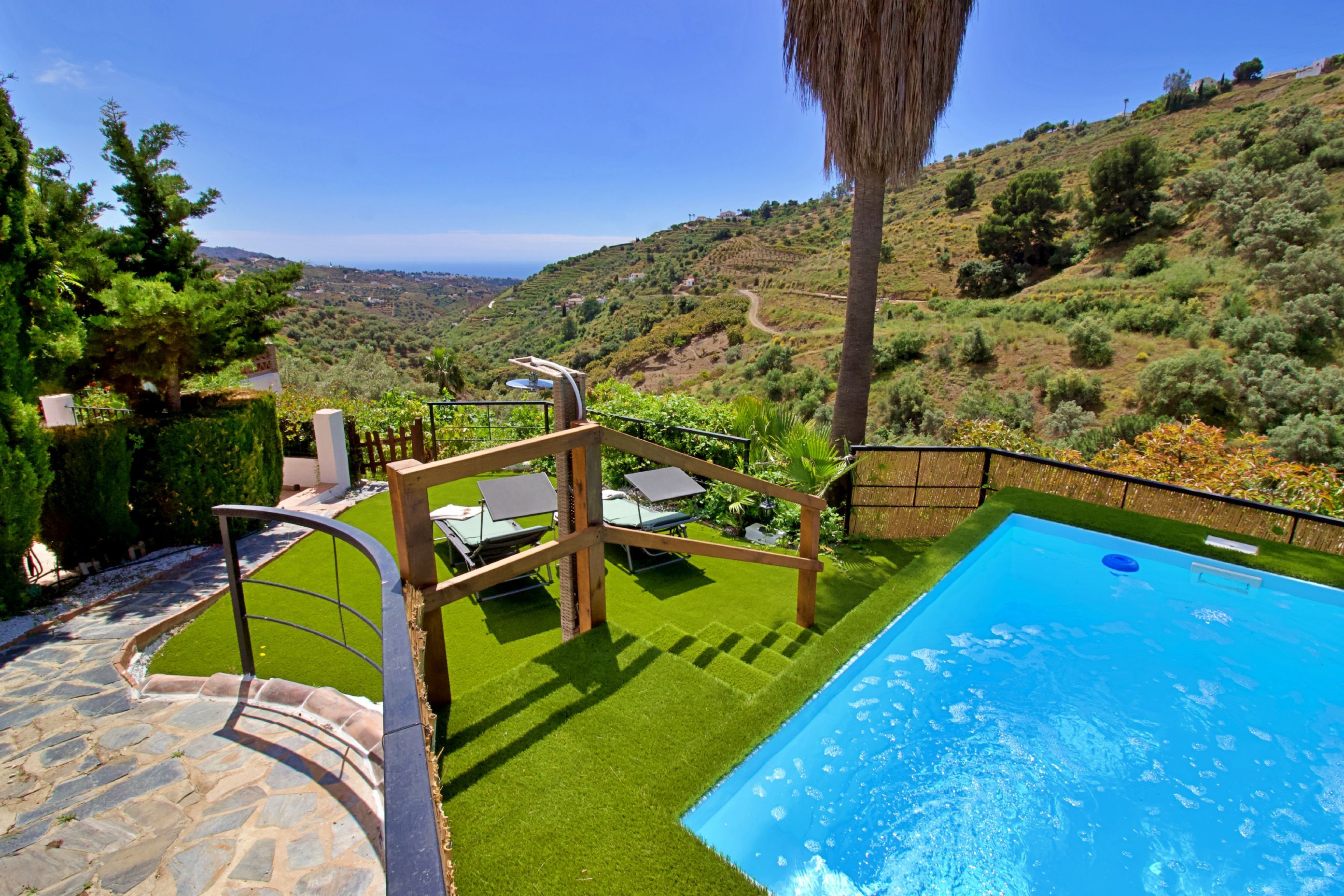 Une piscine bordée d’un chemin de pierre menant à un espace détente avec des chaises longues et offrant une vue sur un paysage vallonné.