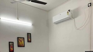 A bedroom with a bed, a ceiling fan, an air conditioning unit, and three framed pictures on the wall. - JP Hotel (Tezpur)