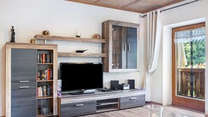 A modern living room with a flat-screen TV, wooden shelves, a cabinet, and a glass coffee table.