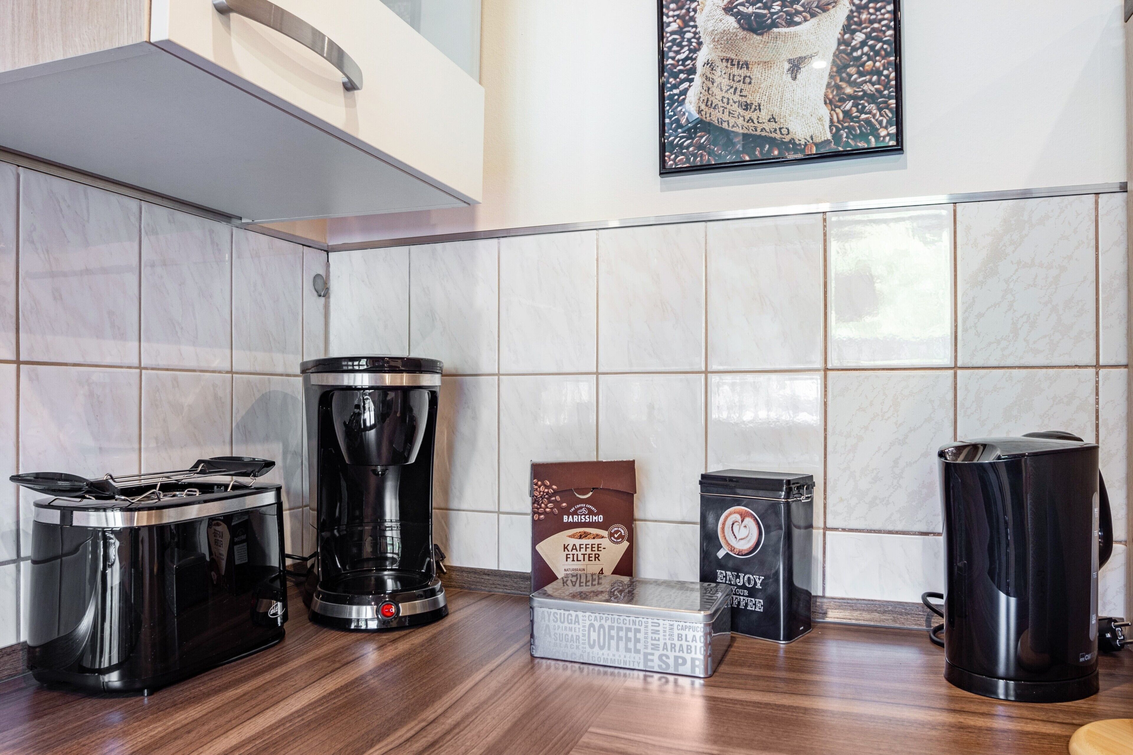 A kitchen with a coffee maker, a box of coffee pods, and a trash can.