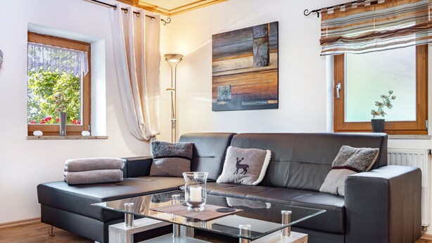 A modern living room with a sofa, glass coffee table, and a window with curtains.