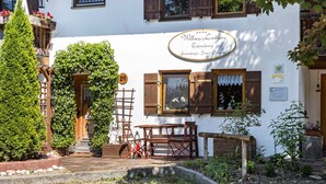 A white building with a sign reading 'Wellness Landhaus,' a wooden bench, and a small table.